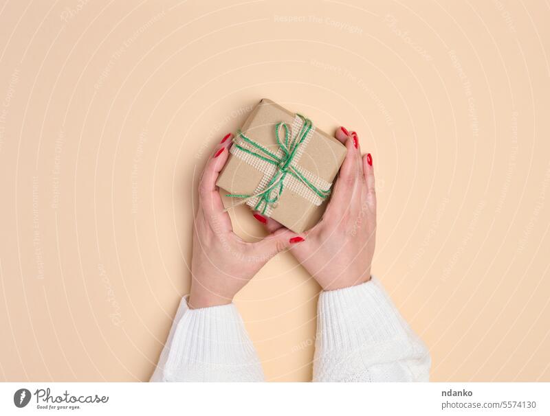 Female hands holding a gift box on a beige background. View from above paper present festive give giving receiving ribbon surprise woman wrapping anniversary