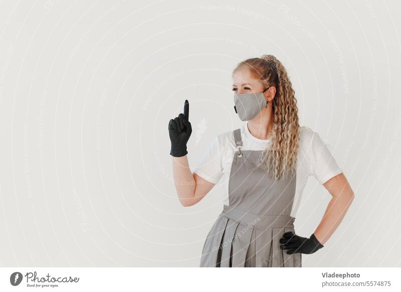 Woman beauty industry master in grey uniform and black gloves shows attention sign on white woman finger young person medicine medical care professional