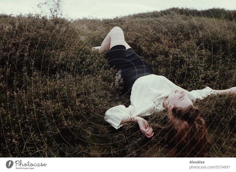 Young woman in white wool sweater and black skirt lying upside down on a rampart in the heath between grass and heather - analog Woman Large tall woman
