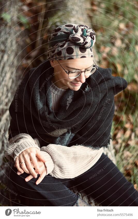 TREE TRUNK - SITTING WOMAN - WAITING Woman 18 - 30 years Headscarf Eyeglasses Autumn Scarf Tree trunk foliage coloured leaves Nature Adults Colour photo
