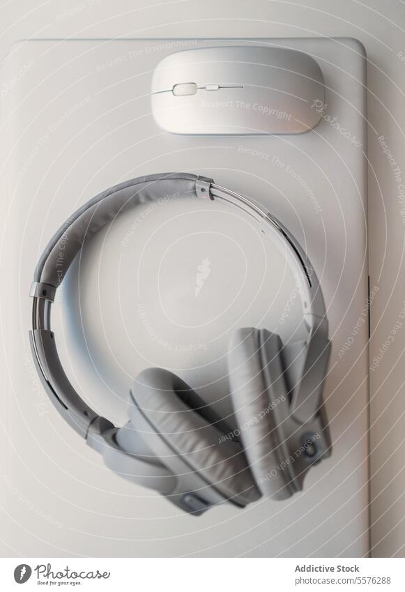 Silver headphones and wireless mouse on laptop silver white computer audio device technology music sound listening accessory desktop equipment over-ear sleek