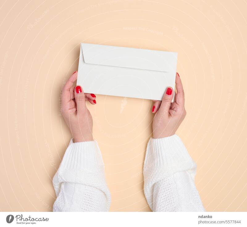Two female hands holding a white rectangular envelope on a beige background, top view letter mail message paper post send showing template woman caucasian adult