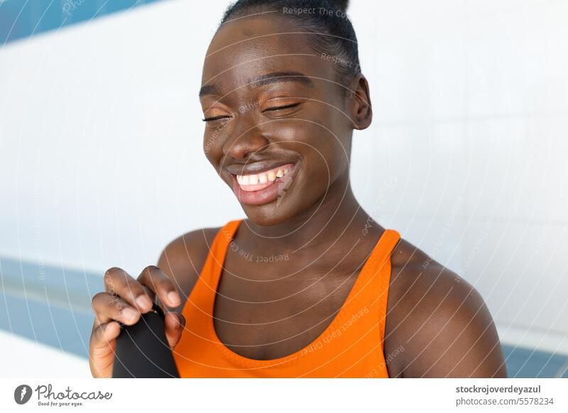 Black young woman smiling and holding her bottle of water, while sitting in a bench at the heated swimming pool female black african person happy american face