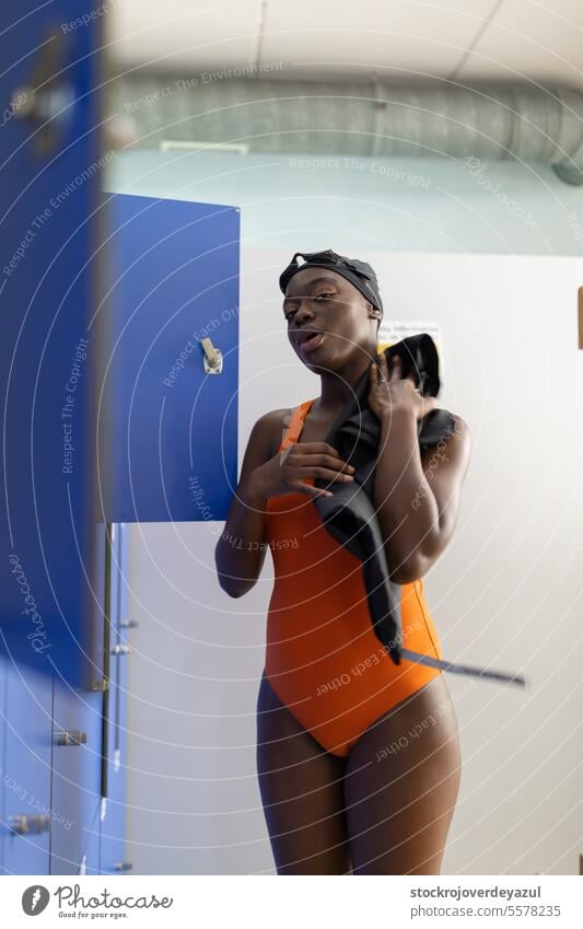 Black young woman toweling off by the lockers in the changing room at swimming pool person fitness black female swimmer towel drying heated swimsuit orange