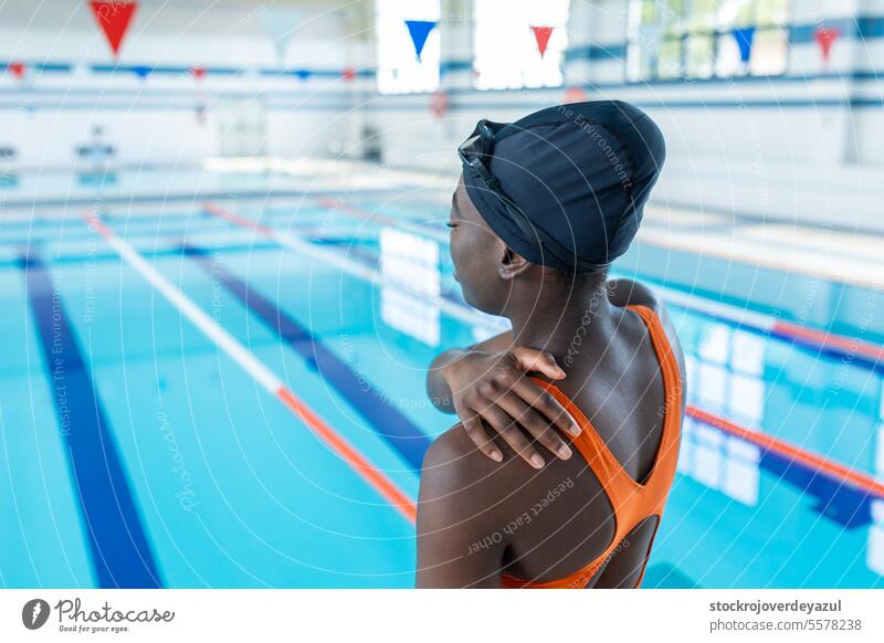 Black young woman touching her sore shoulder at the swimming pool water sport pain injury black female heated swimsuit orange smiling blue lifestyle real people
