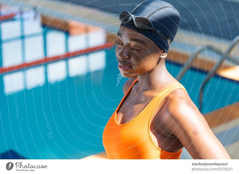 Portrait of a black young woman standing at the swimming pool women female fitness healthy water goggles wet heated orange blue real people wellness happy