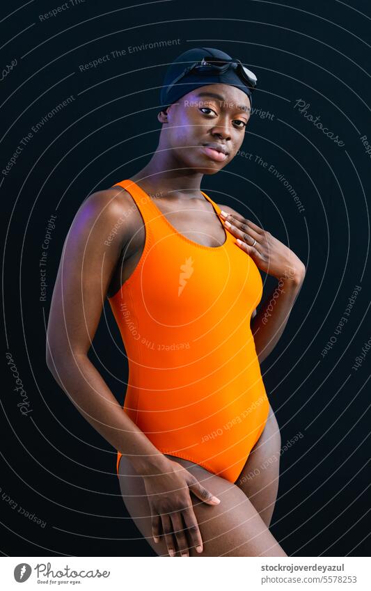 Black young woman in swimsuit posing with plain black background person women female swimming pool heated orange healthy smiling lifestyle real people wellness