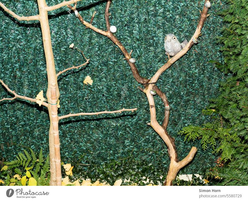 Imitation of a bird sits on artificially arranged branches in front of a wall of plastic leaves imitation Artificial Arranged Bird Set Branches and twigs