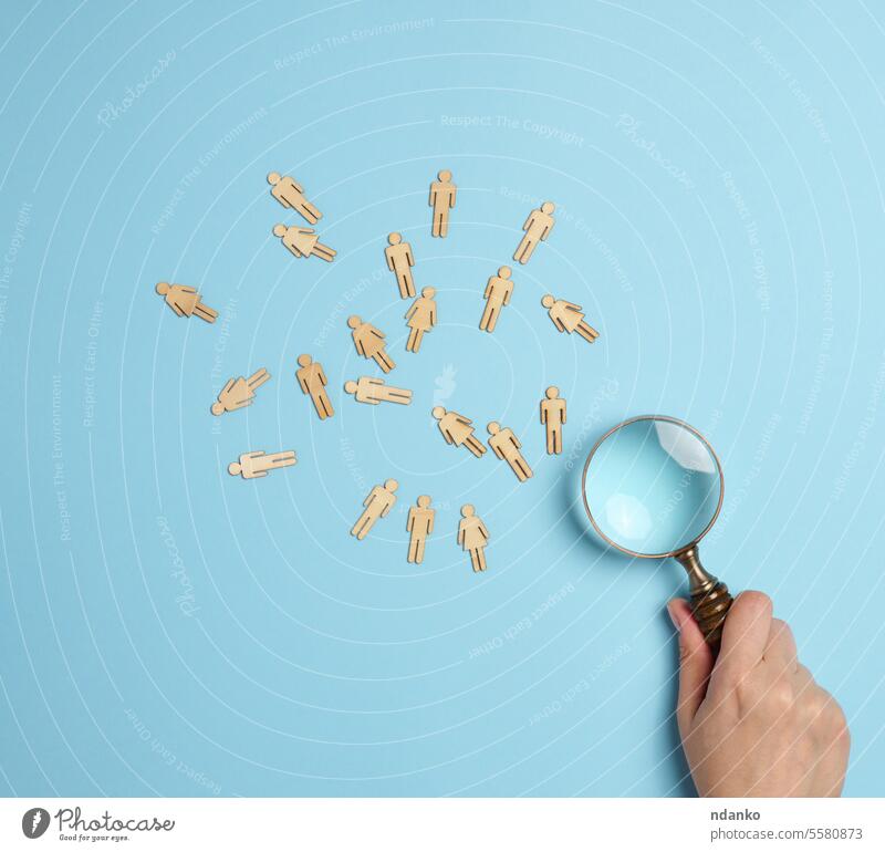 Wooden men and a magnifying glass on a blue background. Recruitment concept, search for talented and capable employees man manager offer recruitment research