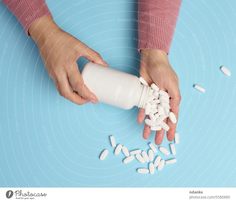 A woman's hand holding a plastic bottle and white oval pills on a blue background, top view. holds medication health care drugs dose concept wellness treatment