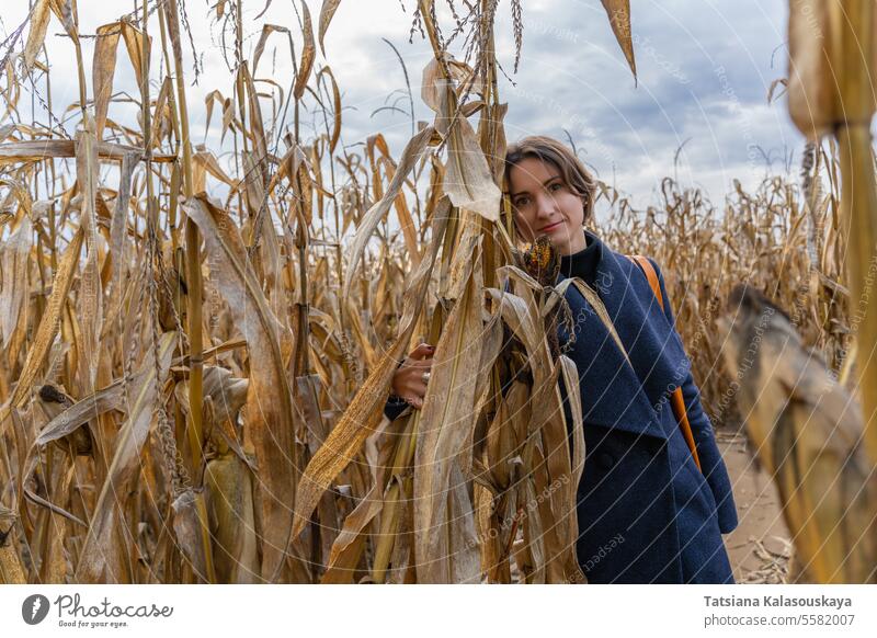 Woman standing in autumn in cornfield and looking at camera woman cornfield. looking at camera coat rows fall outdoors rural countryside harvest seasonal