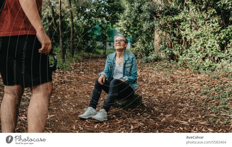 Senior jubilant woman explaining her trip to followers while a guy records her live on social media. retirement person nature streamer modern forest outdoors