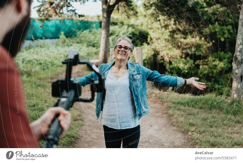 Senior jubilant woman explaining her trip to followers while a guy records her live on social media. senior streamer video retirement women female lifestyle
