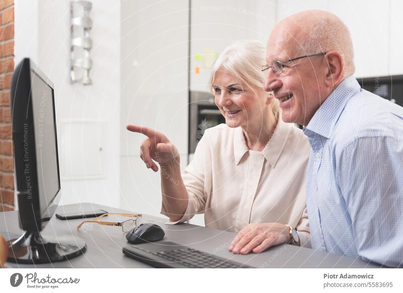 Happy elder couple enjoy together at computer old people senior happy laptop home family person background internet woman table watching photos research view