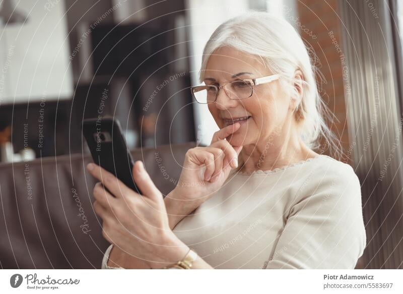 Beautiful senior woman texting at home smartphone elderly smiling pensioner 60s years old aged beautiful casual happy social media technology call chatting