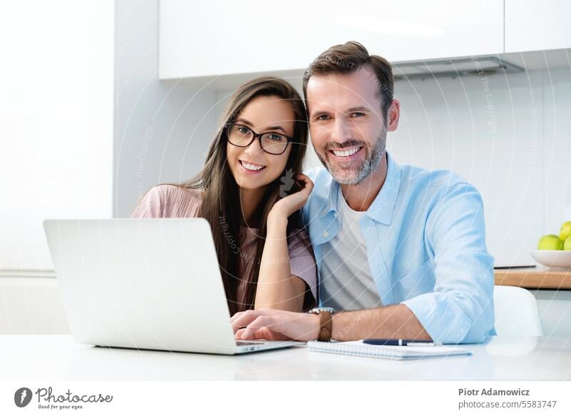 Smiling couple sitting at the computer happy smiling white teeth whitetning perfect smile home laptop budget family financial expenses household accounting