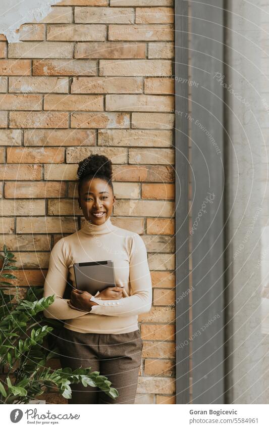 One young African American business woman with digital tablet standing by the brick wall in the industrial style office adult african american black