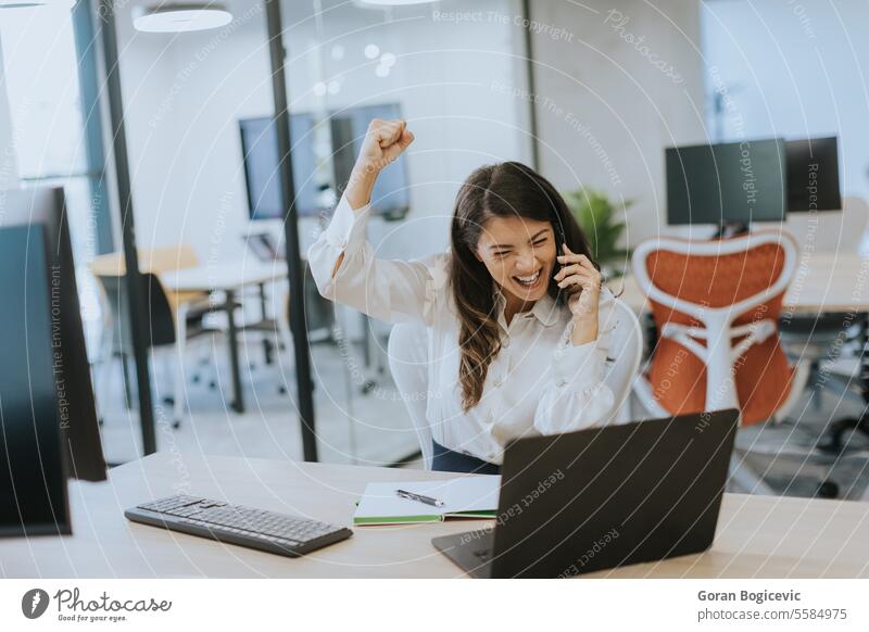 Young business woman using mobile phone while working on laptop in the modern office occupation smartphone young happy talking one person professional beautiful