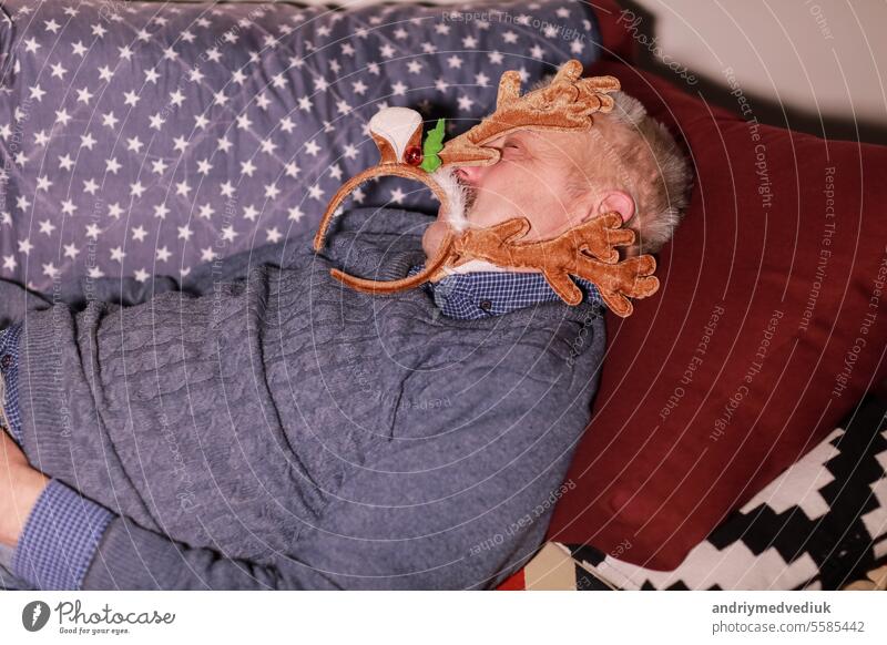 man of 50-60 years sleeping on a sofa wearing decoration in the form of horns of a deer on head. man resting after Christmas and New Years party celebration