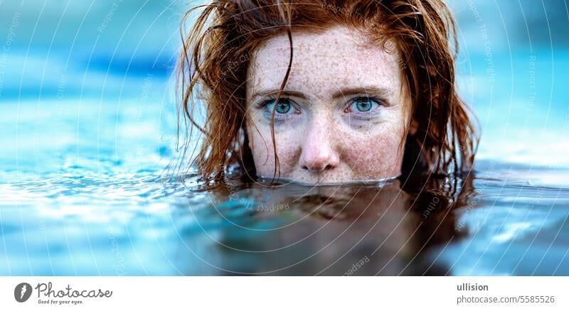 portrait of sexy, young red haired woman with freckles and red wet hair, in turquoise spa pool water, head half under water redhead copy space submerged mermaid