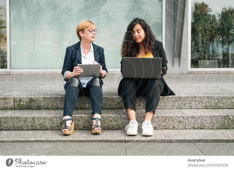 Senior and junior business woman wear business clothes while bonding together. Office worker concept outdoors colleague laptop young sitting computer people