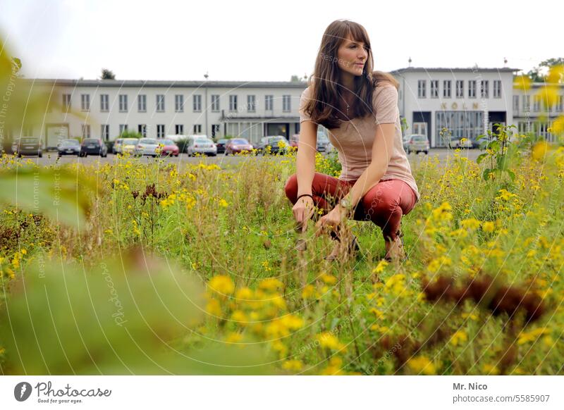 woman naturally Crouch Long-haired Meadow Park Grass Nature Attractive Authentic Environment city greening city park Building Parking lot Observe