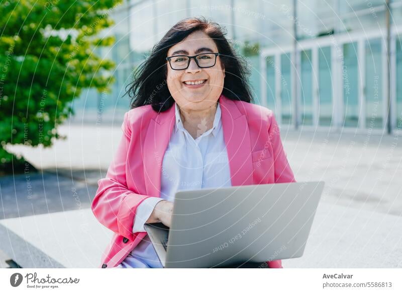 Business jovial adult woman holding a laptop on her lap while smiling and enjoying the fresh air. business women person computer portrait female businesswoman