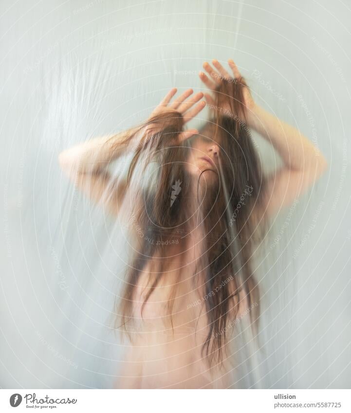 blurred, fuzzy image of sensual romantic young naked sexy woman portrait behind plastic film, playing with her hair, moves in ecstasy nude copy space shy
