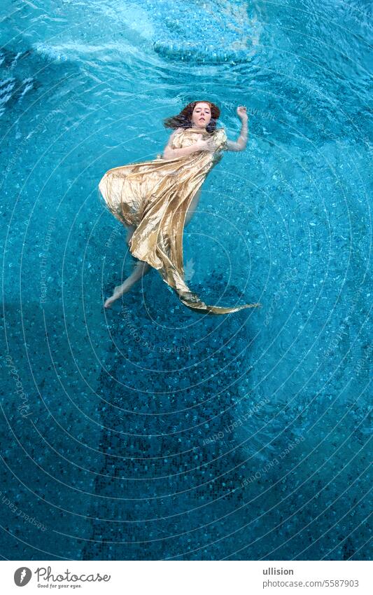 top view to beautiful young sexy redhead woman in golden dress, evening dress, floating weightlessly elegant in the turquoise water in the pool swimming dance