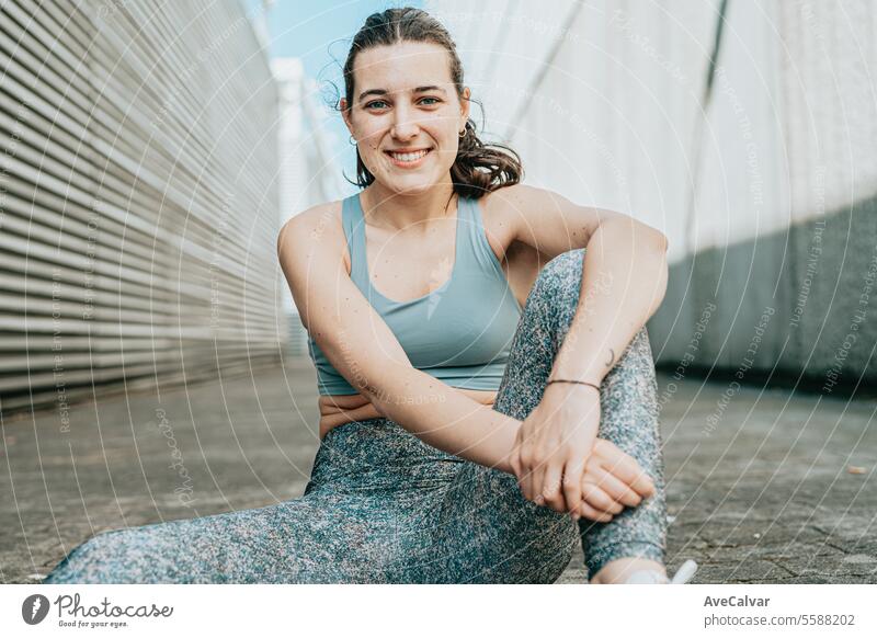 Fit, smiling and cheerful young woman in sportswear sitting on the floor in an urban street scene. female person beauty adult lifestyle fitness outdoor friends