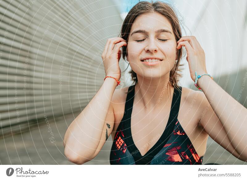 Portrait of a young girl smiling at camera in sportswear touching her hair in an urban setting. female women music person beauty adult lifestyle outdoor friends