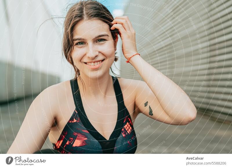 Portrait of a young girl smiling at camera in sportswear touching her hair in an urban setting. woman female person adult beauty lifestyle outdoor friends