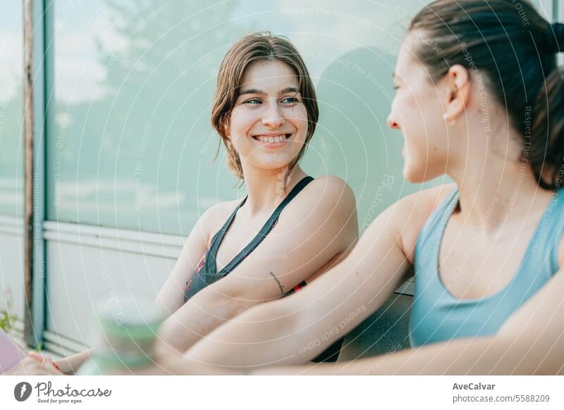 Two young fit cheerful girls sitting rested after doing sports happy to achieve their sports goals. female lifestyle women caucasian two fitness outdoor urban