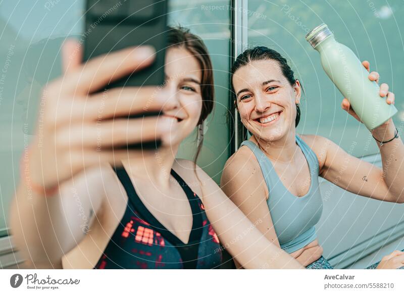Couple of happy friends after having finished training for their favorite sport, taking some selfies with cell phone. female young person mobile lifestyle women