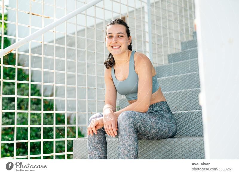 Portrait of a smiling and joyful young girl in sportswear sitting on some stairs. Sport in the city. female women lifestyle healthy fitness person outdoor urban