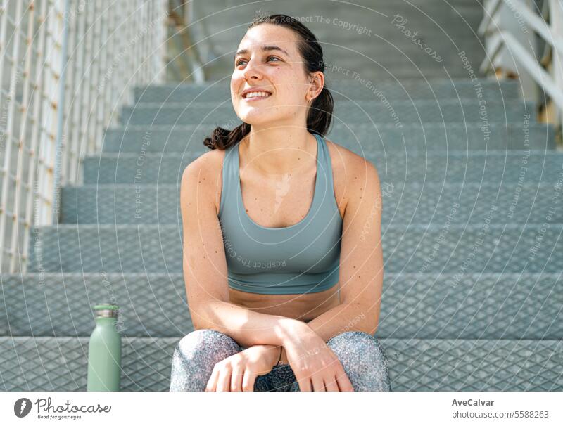 Portrait of a smiling and joyful young girl in sportswear sitting on some stairs. Sport in the city. athletic lifestyle fitness women female outdoor urban