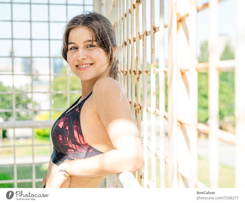 Sporty and healthy young smiling woman leaning on a white fence in an urban environment. female women person summer beauty pretty lifestyle outdoor friends