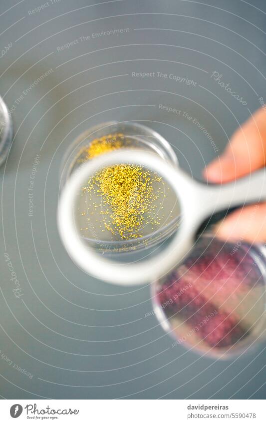 Female chemist hand holding magnifying glass to analyze golden glitter sample on petri dish in lab female analysis laboratory magnification lens close up