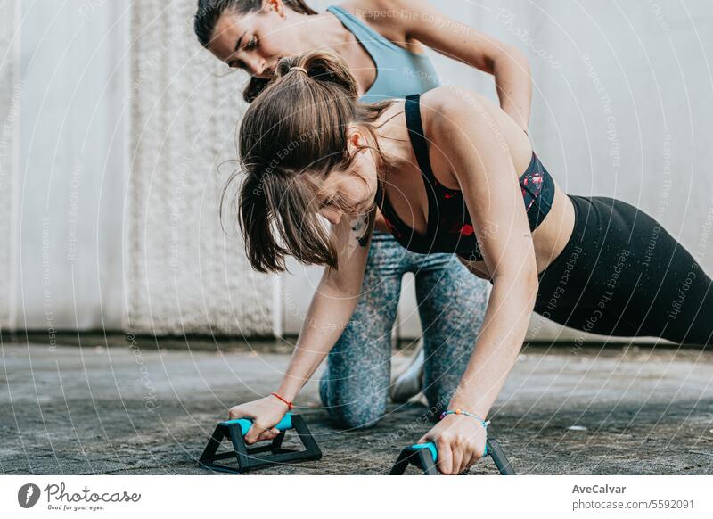 Two young girls helping each other do push-ups,being careful with their posture to strengthen muscle sport training women outdoor urban friends fitness athletic