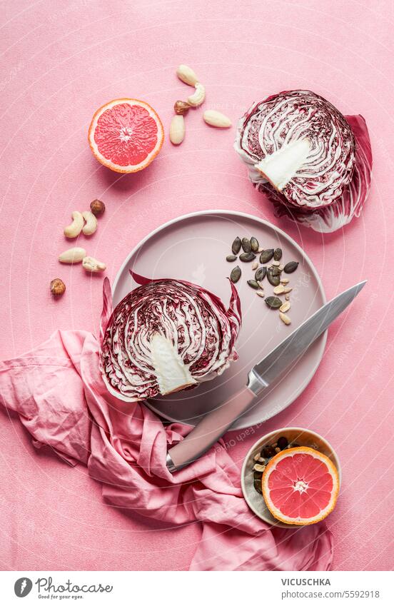 Ingredients for healthy salad with radicchio lettuce, grapefruit and nuts with plate and knife on pink background, top view ingredients copy space