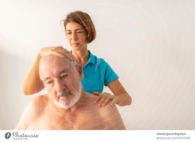 A female physiotherapist performs stretches on the neck of her patient, an elderly man, to aid in his rehabilitation and wellbeing treatment manual therapy