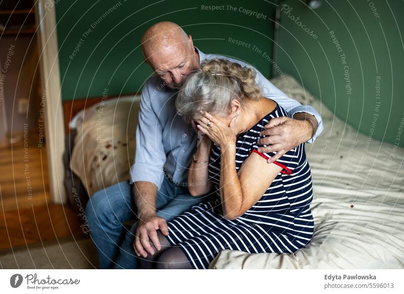 Senior husband consoling his depressed wife at home real people woman senior mature female couple together elderly house old aging pensioner grandparents
