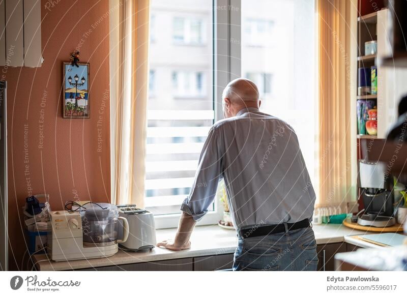 Senior man standing at the kitchen counter in his house and looking out the window real people senior senior adult mature male Caucasian elderly home old aging