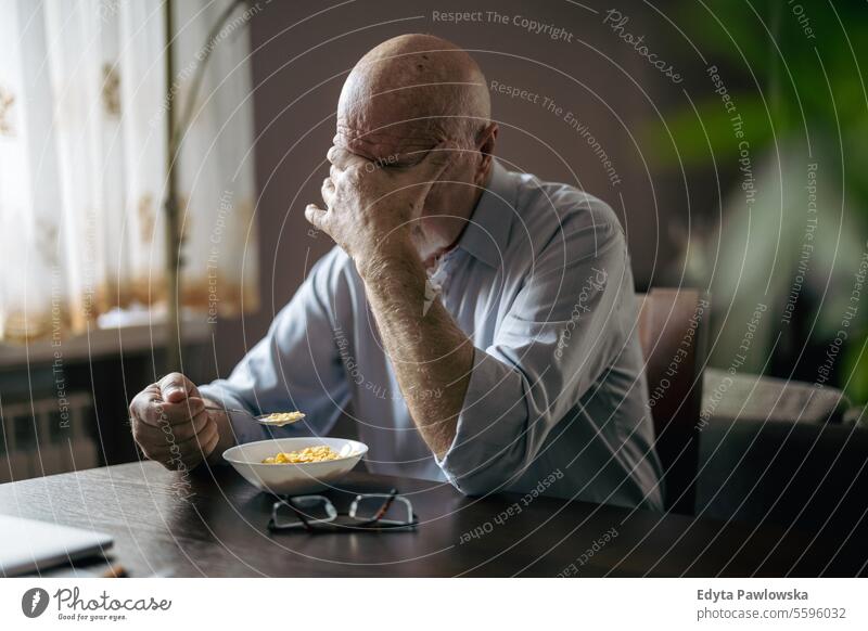Depressed senior man eating breakfast alone at home real people senior adult mature male Caucasian elderly house old aging domestic life grandfather pensioner