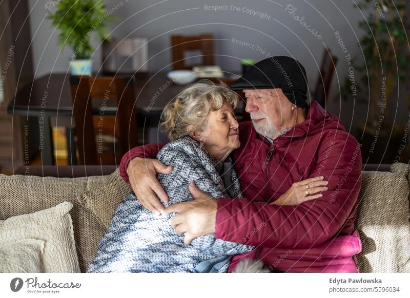 Senior couple wearing winter clothing inside home due to high electricity prices cold temperature warm clothing uncomfortable sadness frozen energy efficient