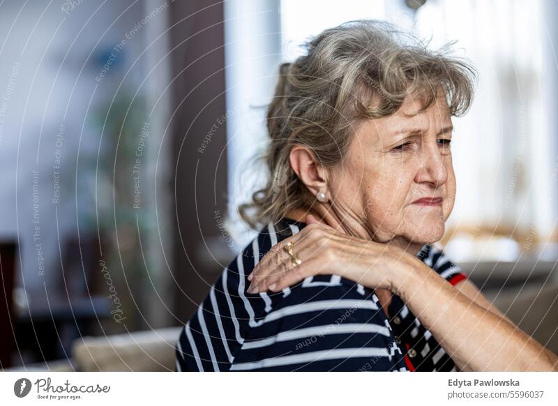 Portrait of senior woman suffering from neck pain while sitting on sofa at home real people mature female Caucasian elderly house old aging domestic life
