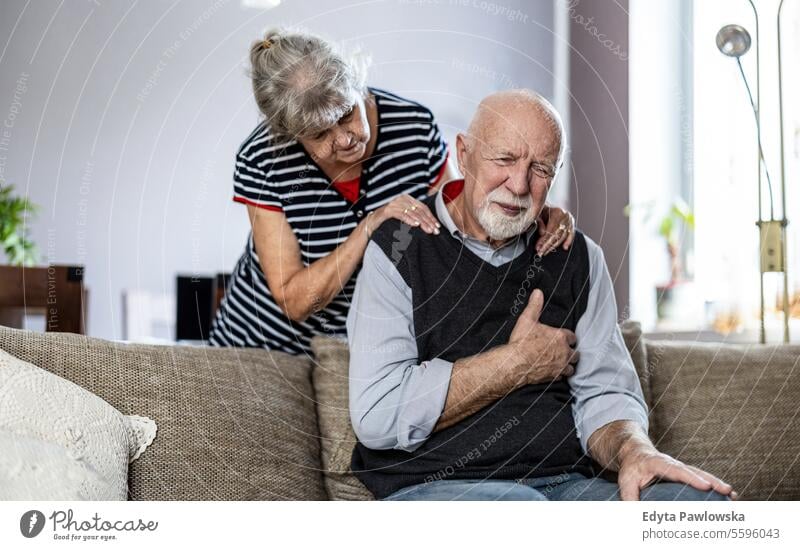 Senior man suffering from chest pain while his wife comforting him real people woman senior mature female couple together Caucasian elderly home house old aging