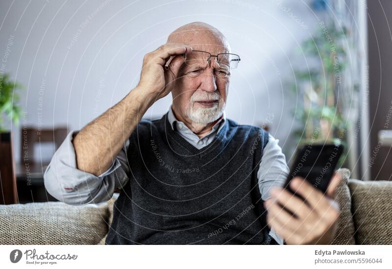 Senior man staring at his smartphone in confusion real people senior senior adult mature male Caucasian elderly home house old aging domestic life grandfather
