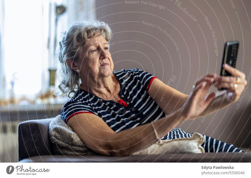 Elderly woman sitting on couch and using mobile phone at home real people senior mature female Caucasian elderly house old aging domestic life grandmother