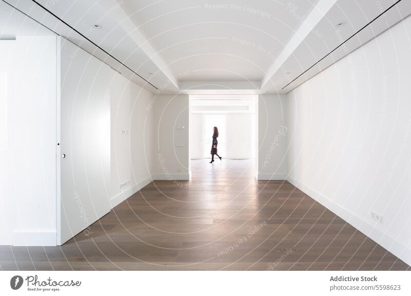 Minimalist hallway with hardwood floors and an unrecognizable woman walking through, surrounded by white walls and natural light Hallway minimalist person